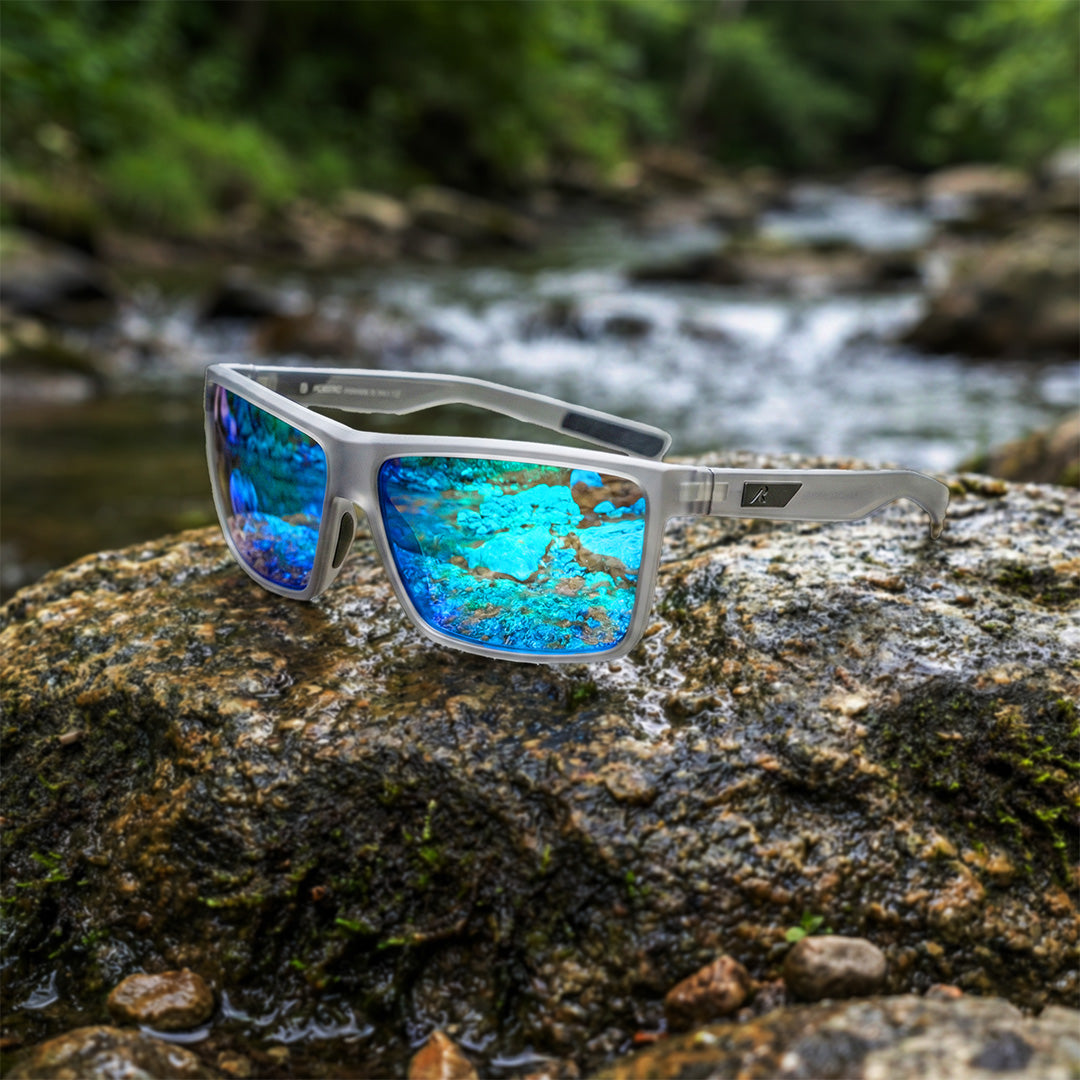 Sunglasses with blue reflective lenses on a rock by a stream